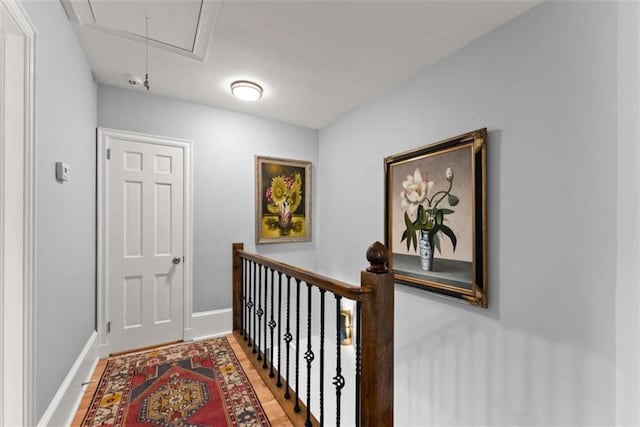 hall featuring attic access, baseboards, wood finished floors, and an upstairs landing