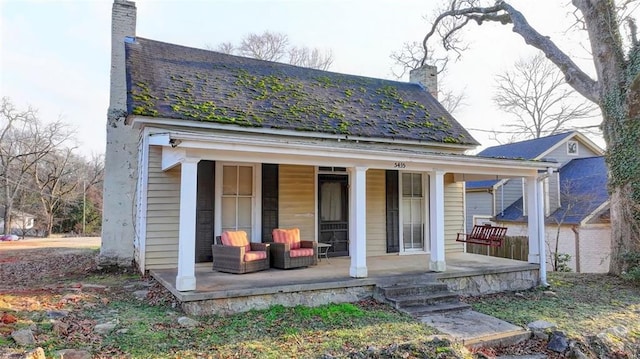 rear view of house with covered porch, a shingled roof, and a chimney