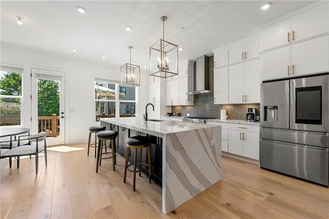 kitchen with backsplash, wall chimney range hood, light wood-style flooring, stainless steel refrigerator with ice dispenser, and a sink