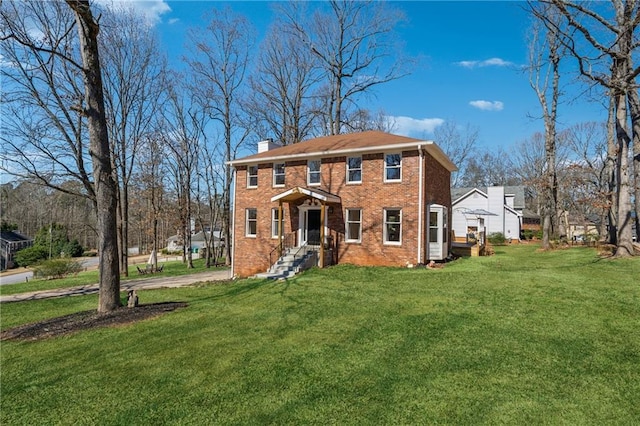 colonial home with a front yard, a chimney, and brick siding