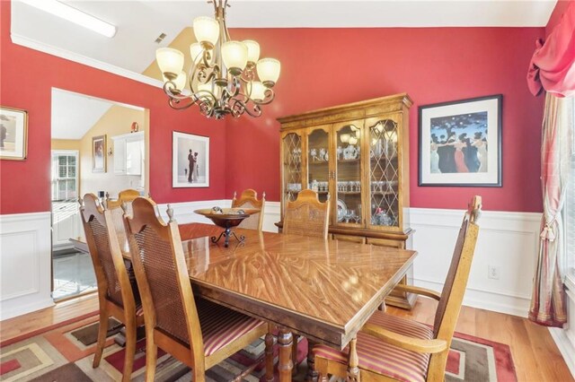 dining area with light hardwood / wood-style floors, crown molding, lofted ceiling, and an inviting chandelier