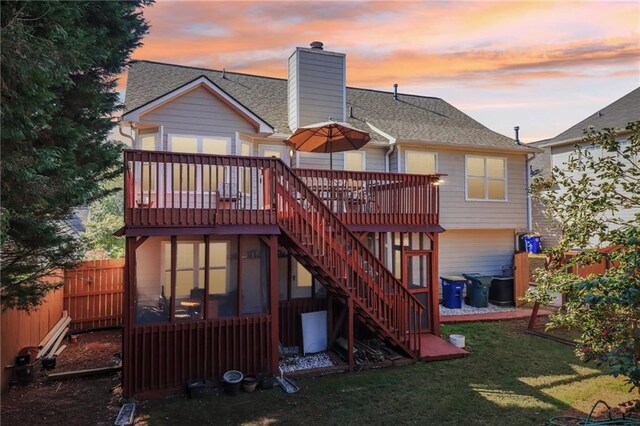 back house at dusk featuring a wooden deck and a lawn