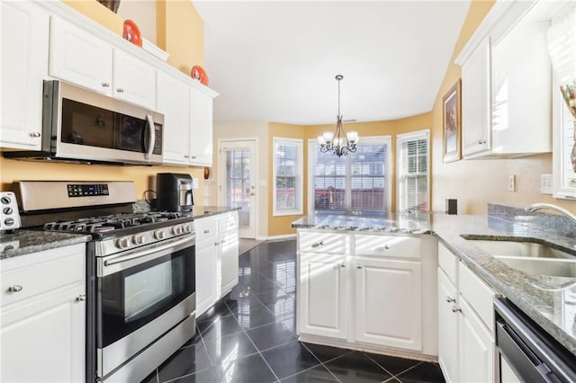 kitchen with appliances with stainless steel finishes, kitchen peninsula, white cabinets, and a chandelier