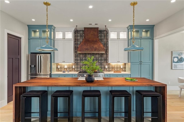 kitchen with butcher block countertops, stove, stainless steel fridge, and custom exhaust hood