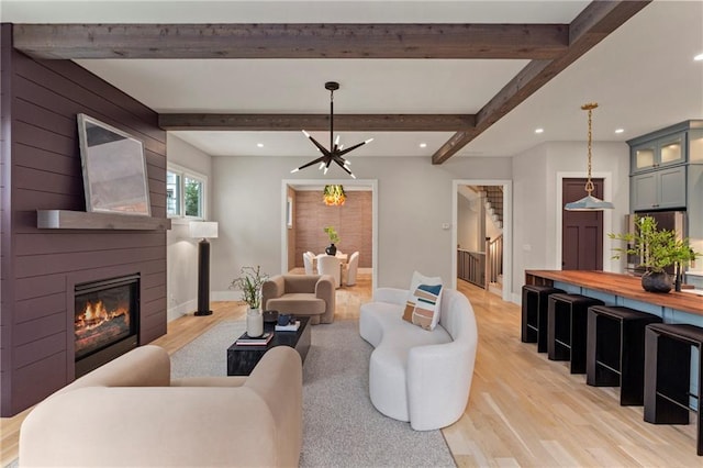 living room with light wood-type flooring, a large fireplace, beamed ceiling, and stairway