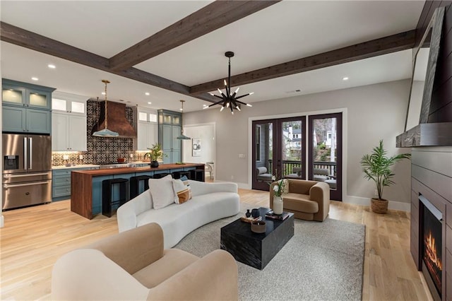 living room with a notable chandelier, a fireplace, baseboards, light wood-style floors, and beamed ceiling