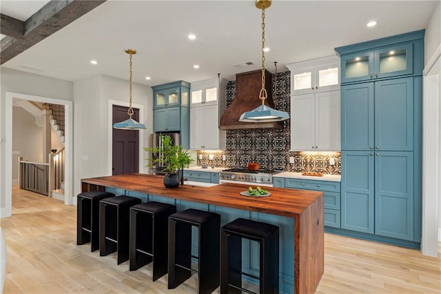 kitchen with blue cabinets, premium range hood, wood counters, stainless steel gas range, and backsplash