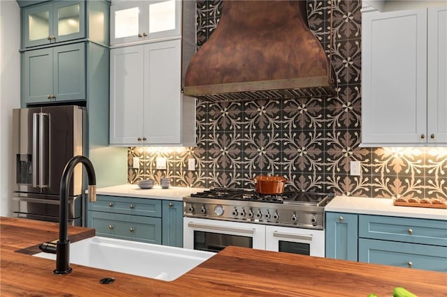 kitchen featuring tasteful backsplash, appliances with stainless steel finishes, glass insert cabinets, a sink, and premium range hood