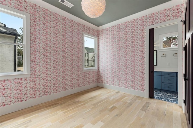 empty room with baseboards, visible vents, light wood finished floors, and wallpapered walls