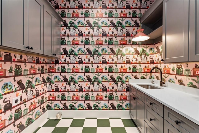 kitchen featuring wallpapered walls, tile patterned floors, light countertops, gray cabinetry, and a sink