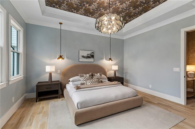 bedroom with light wood finished floors, a tray ceiling, and baseboards