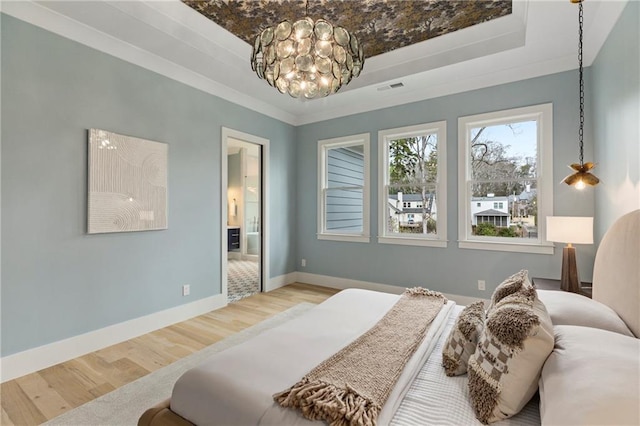 bedroom with a tray ceiling, visible vents, baseboards, and wood finished floors