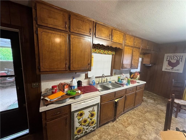 kitchen featuring dishwasher, a sink, light countertops, a textured ceiling, and wooden walls