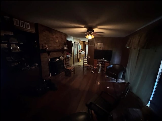 living area featuring a ceiling fan, wood finished floors, and a brick fireplace