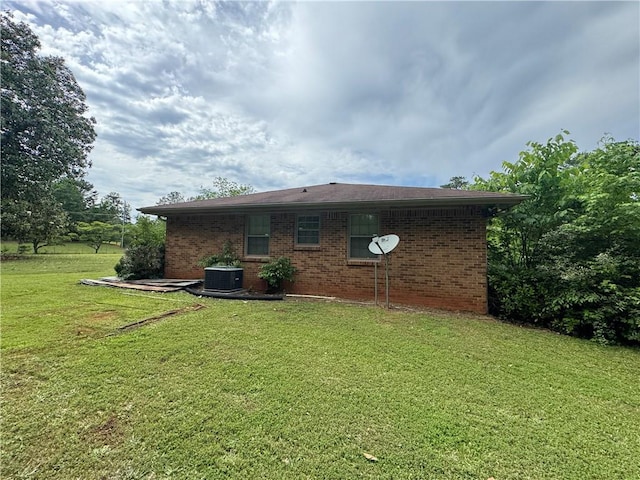 rear view of house with brick siding, a yard, and central AC