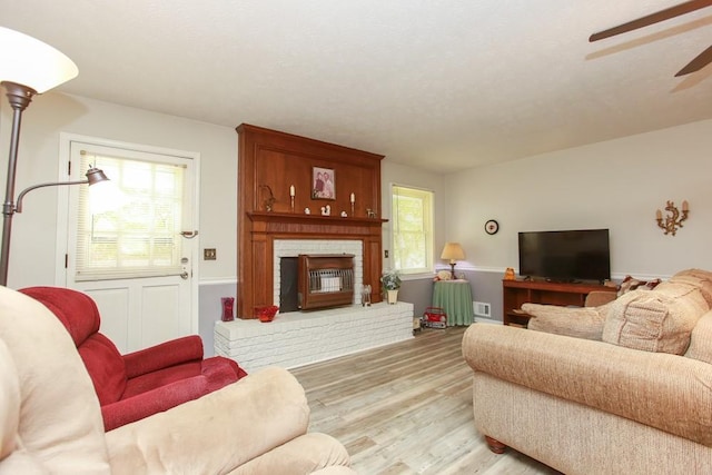 living room with ceiling fan, a brick fireplace, and light hardwood / wood-style flooring