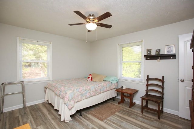 bedroom with ceiling fan, a textured ceiling, hardwood / wood-style flooring, and multiple windows