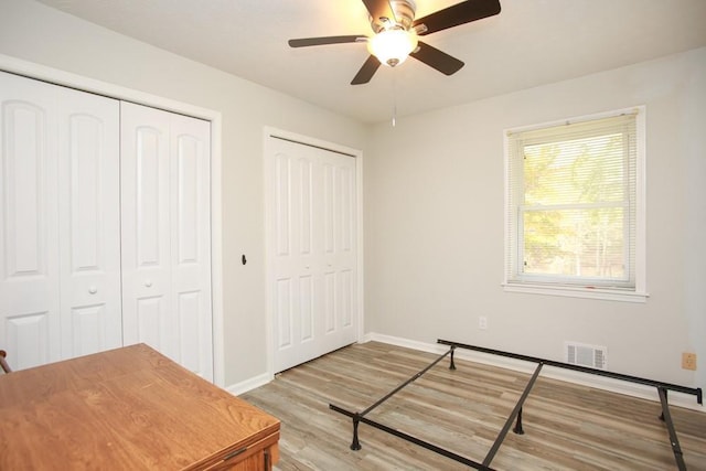 unfurnished bedroom featuring ceiling fan, two closets, and light wood-type flooring