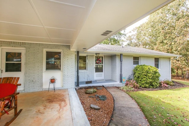 view of exterior entry featuring a porch, a patio area, and a yard