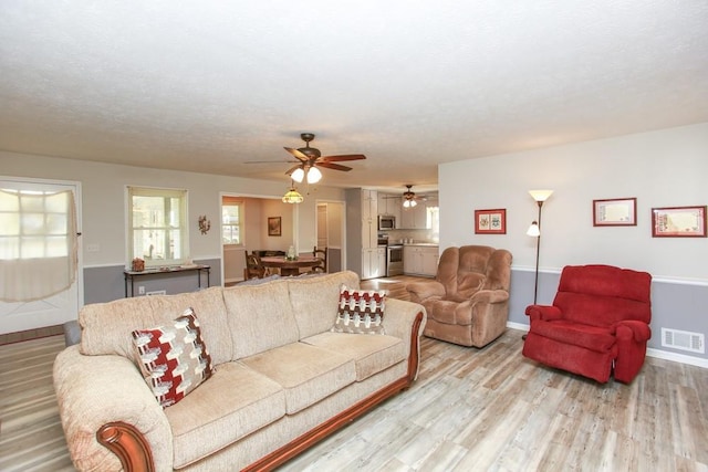 living room with a textured ceiling, baseboards, visible vents, and light wood-type flooring