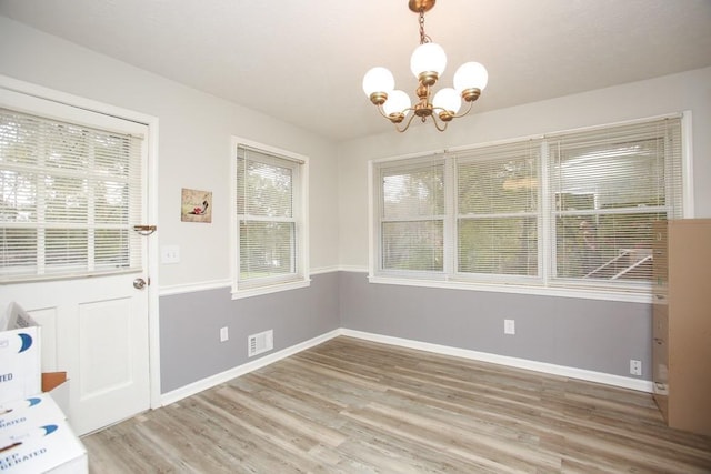 unfurnished dining area featuring wood-type flooring and an inviting chandelier