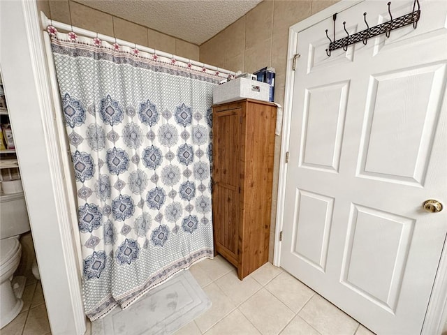 bathroom with a textured ceiling, a shower with shower curtain, toilet, tile walls, and tile patterned flooring
