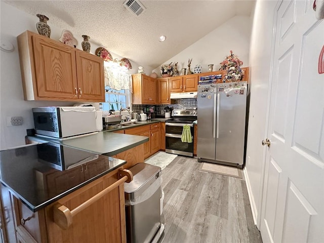 kitchen featuring appliances with stainless steel finishes, visible vents, dark countertops, under cabinet range hood, and vaulted ceiling