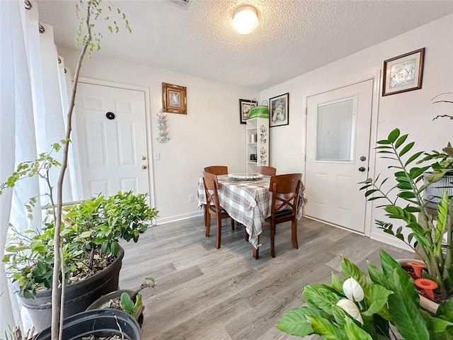 dining space with light wood finished floors, a textured ceiling, and baseboards