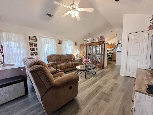 living room featuring a ceiling fan, visible vents, wood finished floors, and lofted ceiling