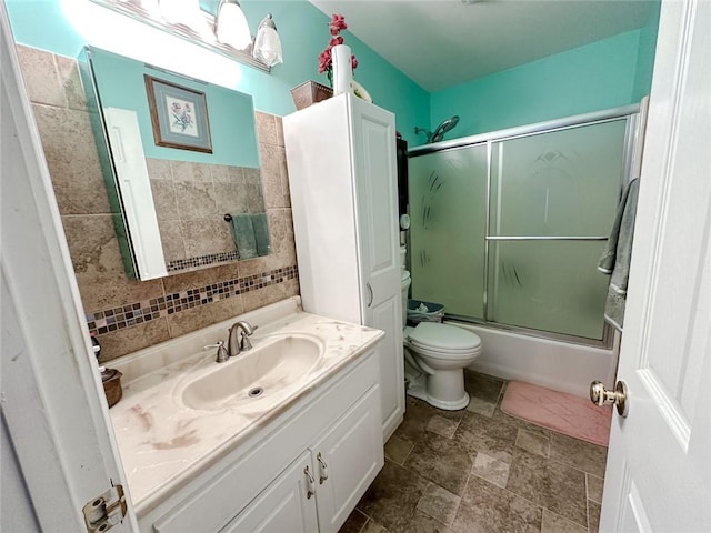 full bathroom featuring stone finish flooring, vanity, toilet, and shower / bath combination with glass door