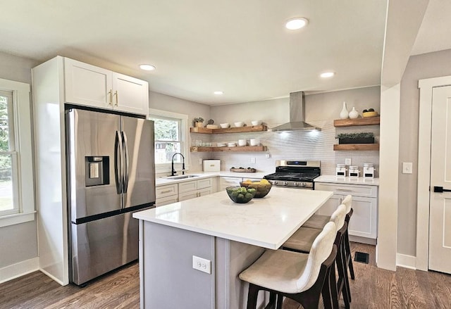 kitchen with stainless steel appliances, open shelves, wall chimney exhaust hood, and a sink