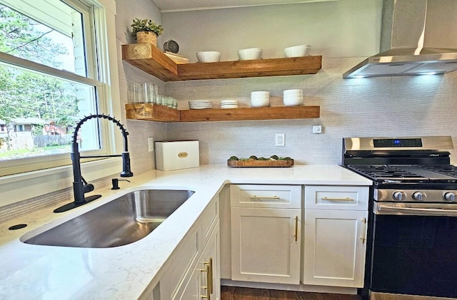 kitchen featuring wall chimney range hood, open shelves, gas stove, and a sink