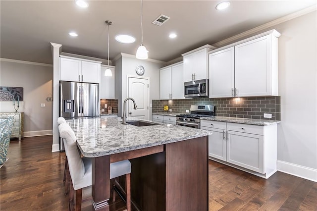 kitchen featuring stainless steel appliances, dark wood-type flooring, a sink, visible vents, and a center island with sink