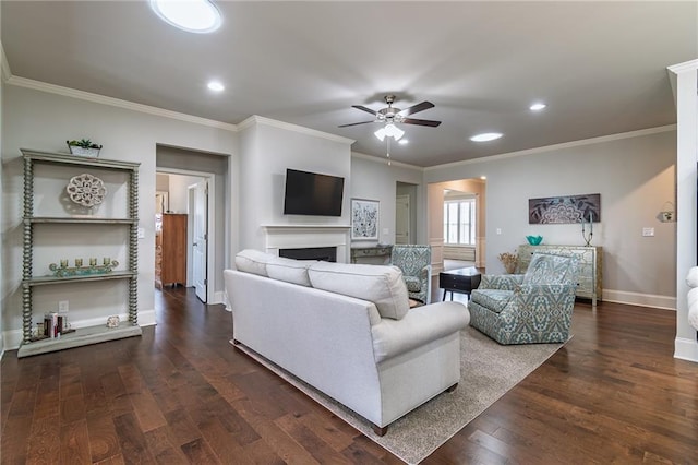 living room featuring baseboards, dark wood finished floors, a ceiling fan, crown molding, and a fireplace