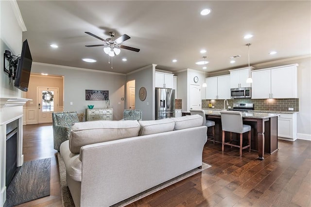 living area with crown molding, a fireplace, dark wood finished floors, recessed lighting, and ceiling fan