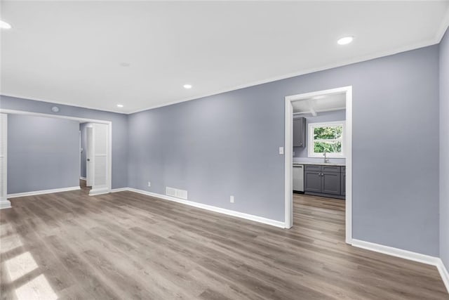 spare room with crown molding, visible vents, a sink, wood finished floors, and baseboards