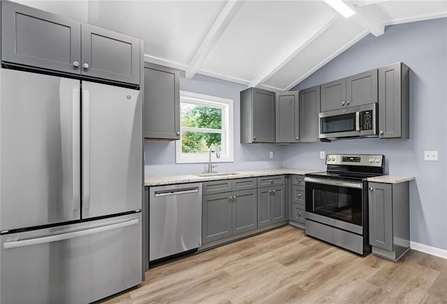 kitchen with light wood-style flooring, vaulted ceiling with beams, stainless steel appliances, gray cabinetry, and a sink