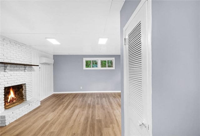 unfurnished living room featuring a wall unit AC, a brick fireplace, light wood-type flooring, and baseboards