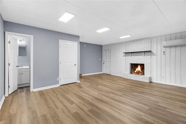 unfurnished living room with a wall mounted AC, sink, light hardwood / wood-style flooring, and a brick fireplace