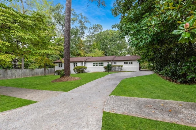 ranch-style home featuring driveway, fence, and a front yard