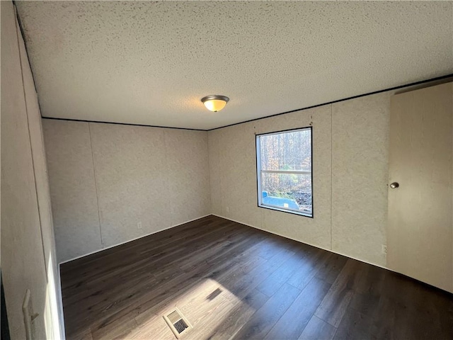 spare room featuring visible vents, dark wood-type flooring, and a textured ceiling