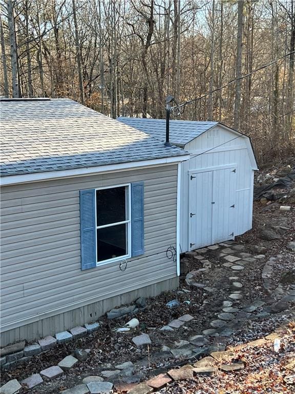 view of side of home with a forest view, a storage unit, an outdoor structure, and a shingled roof