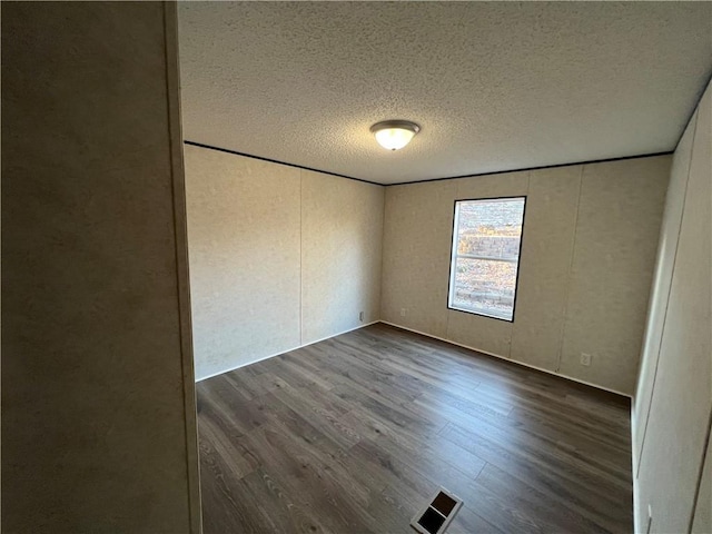 empty room with visible vents, a textured ceiling, and wood finished floors