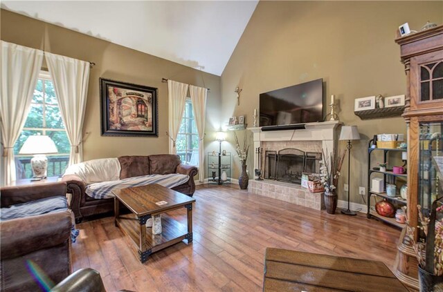 living room with hardwood / wood-style flooring, a fireplace with raised hearth, healthy amount of natural light, and high vaulted ceiling