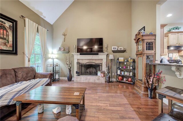 living room featuring wood-type flooring, a brick fireplace, high vaulted ceiling, and recessed lighting