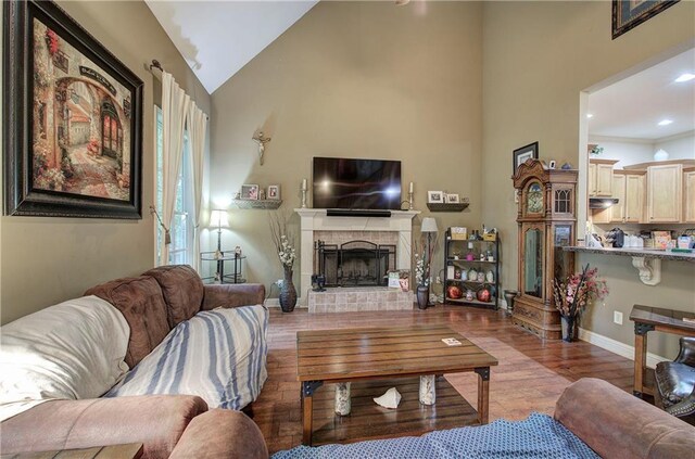 living room with wood finished floors, a fireplace with raised hearth, high vaulted ceiling, baseboards, and recessed lighting