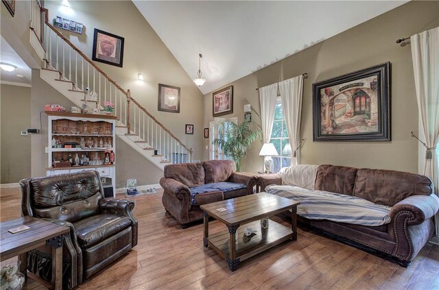 living room featuring stairway, wood-type flooring, high vaulted ceiling, and baseboards