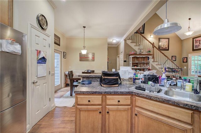 kitchen with freestanding refrigerator, light wood finished floors, ornamental molding, a sink, and decorative light fixtures