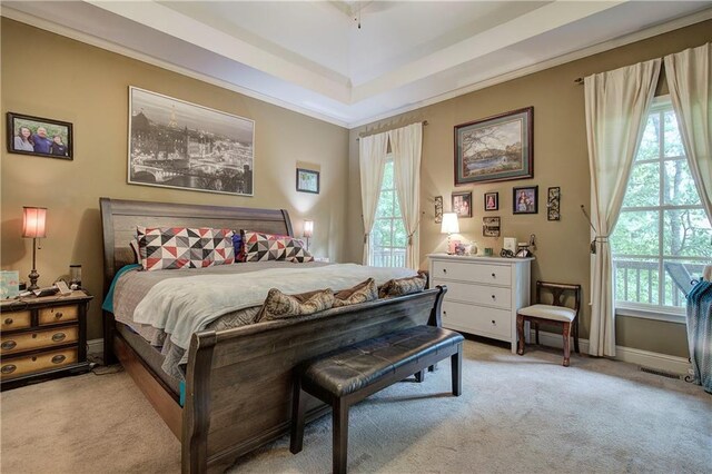 bedroom featuring light carpet, multiple windows, ornamental molding, and a tray ceiling