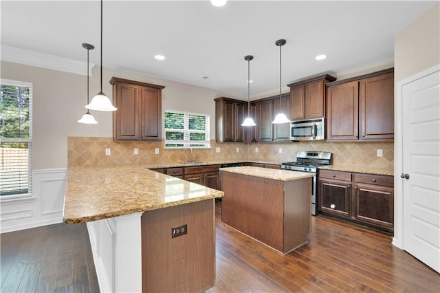 kitchen with crown molding, light stone countertops, a peninsula, stainless steel appliances, and dark wood-type flooring